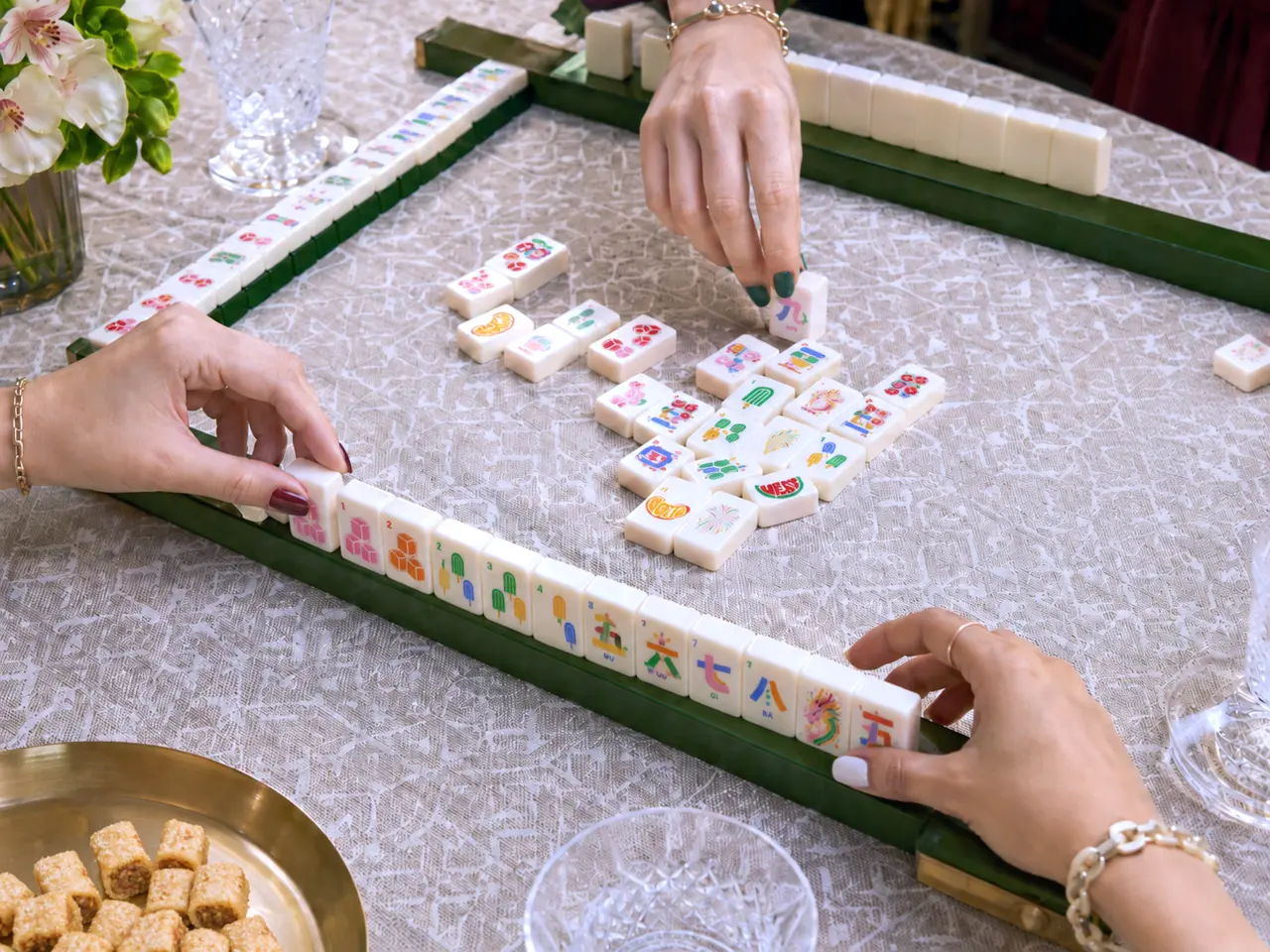 Women with colorful manicures playing American Mahjong at an elegant table